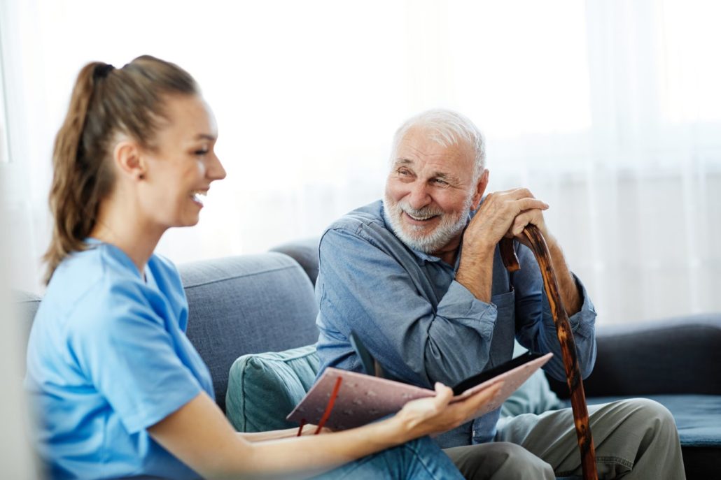 Doctor or nurse caregiver with senior man looking at photo album and picture  at home or nursing home