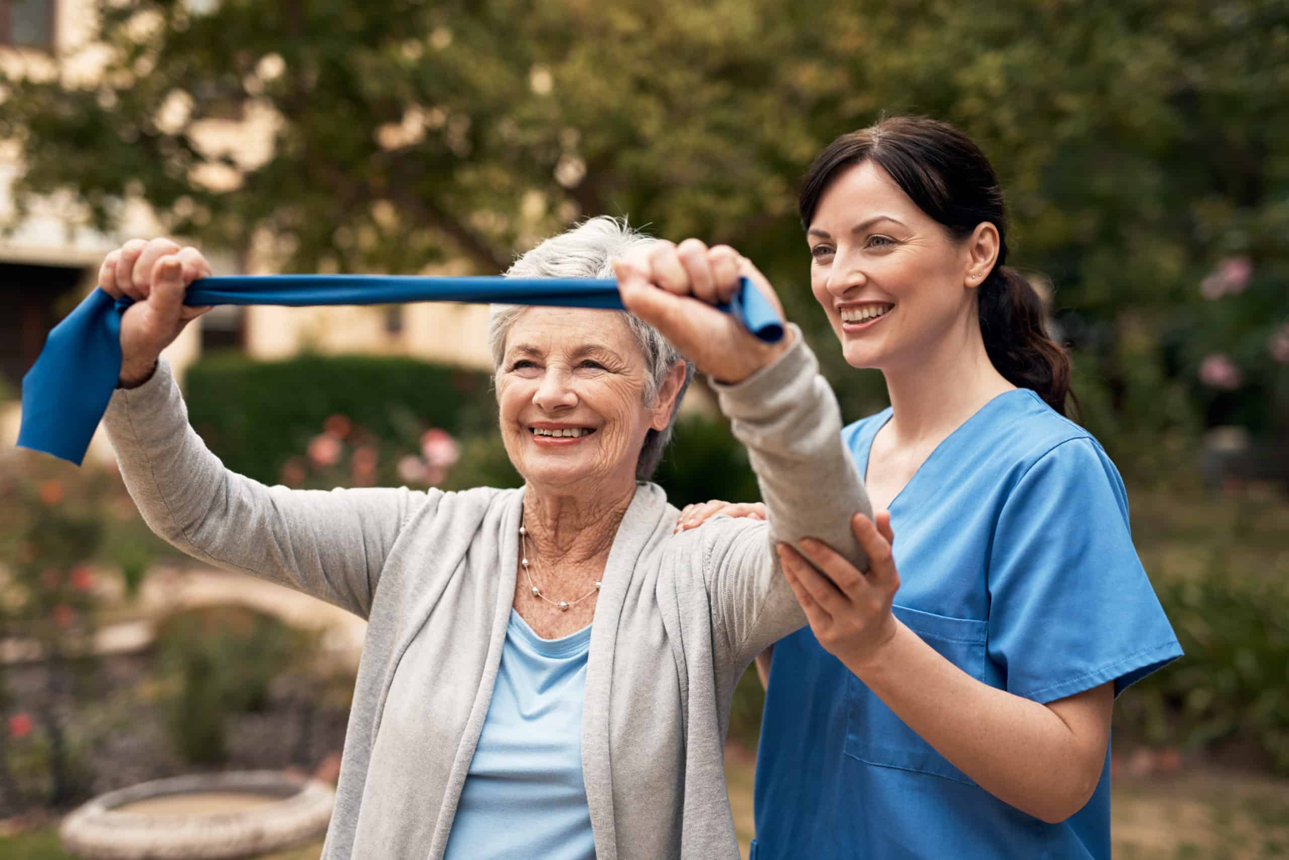 Older woman using resistance bands with the help of a younger female assistant